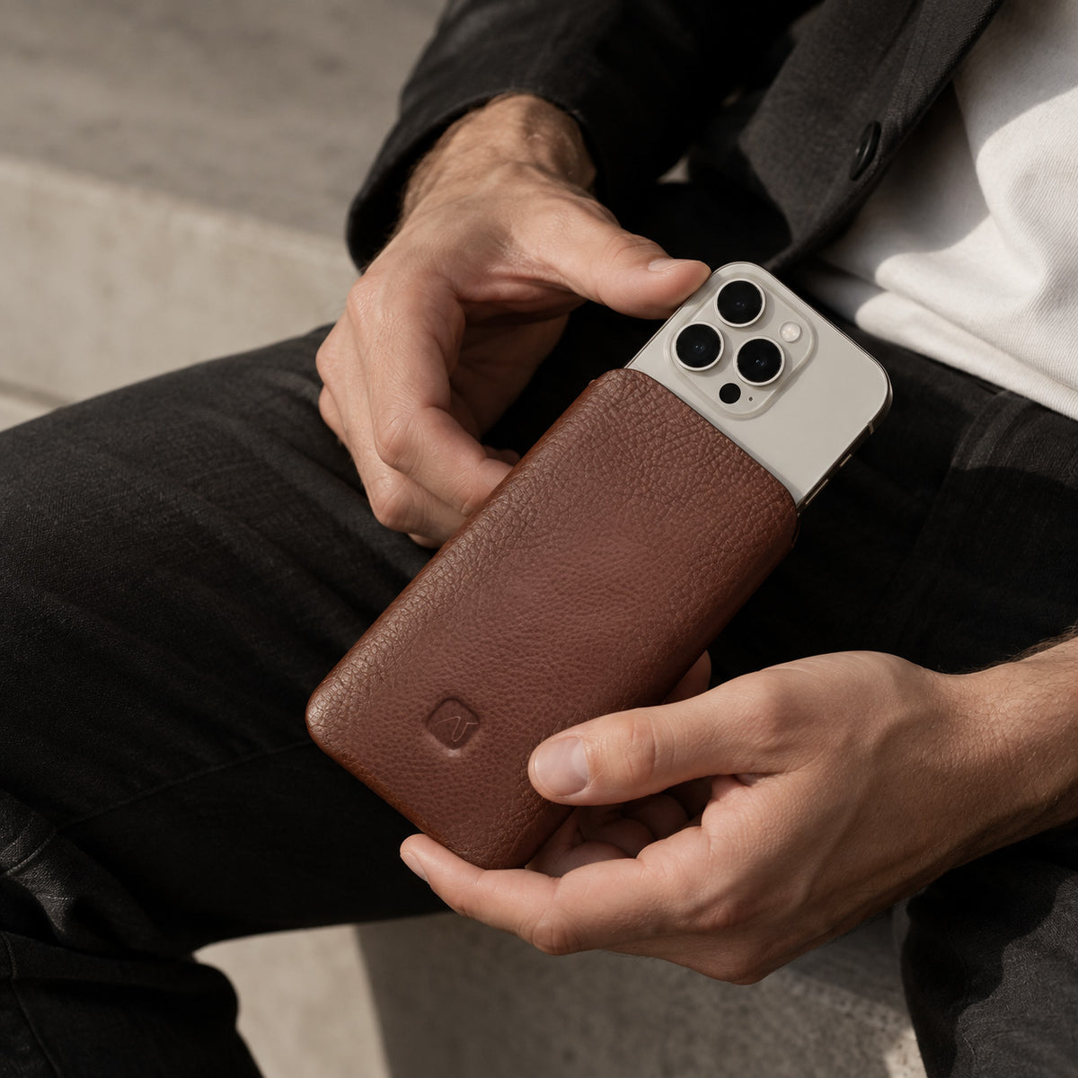 Männerhände halten eine nussbraune Leder Handyhülle in der Hand und schieben ein iPhone hinein.