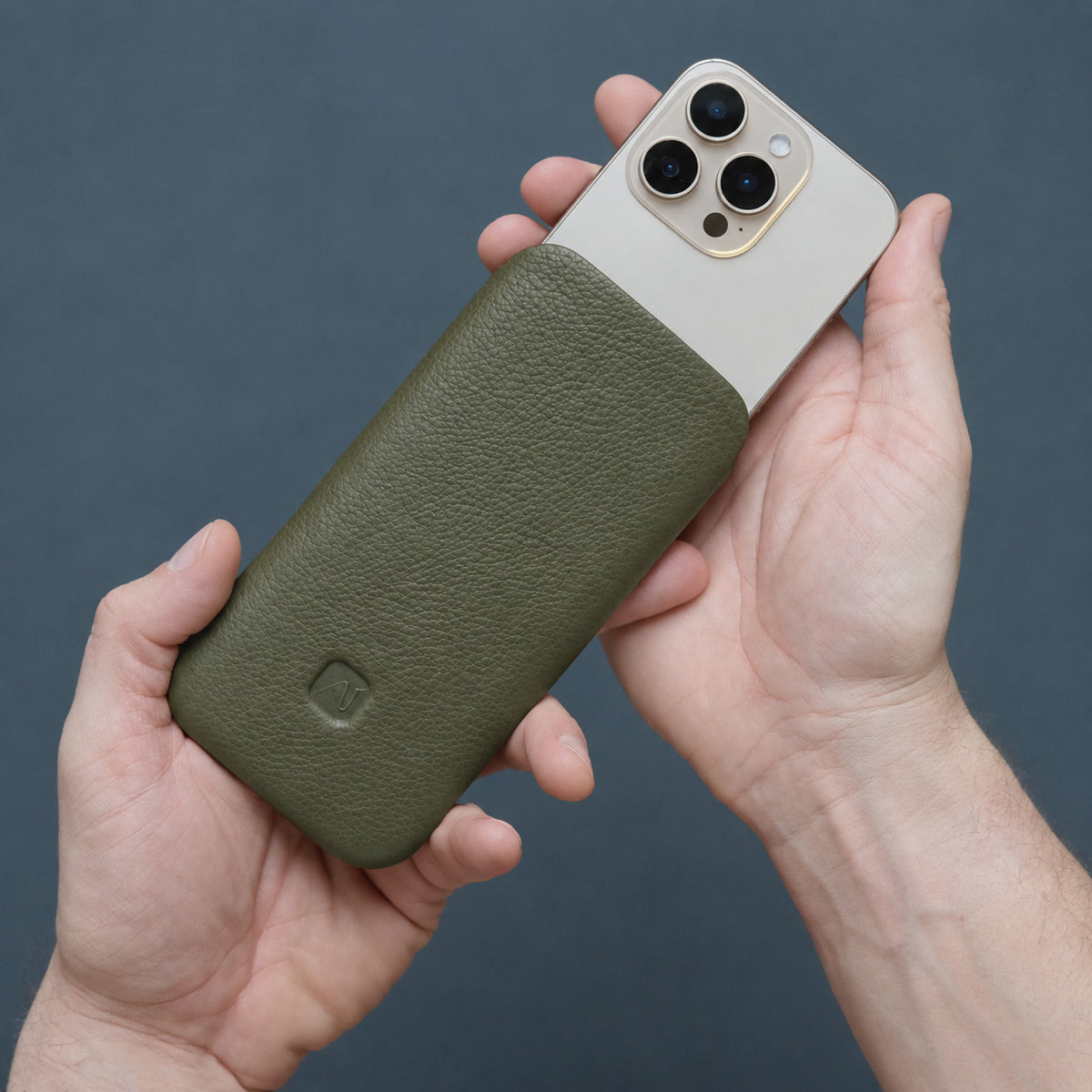 Männerhände halten eine olivgrüne Handyhülle aus Leder, aus dem sie ein iPhone herausziehen
