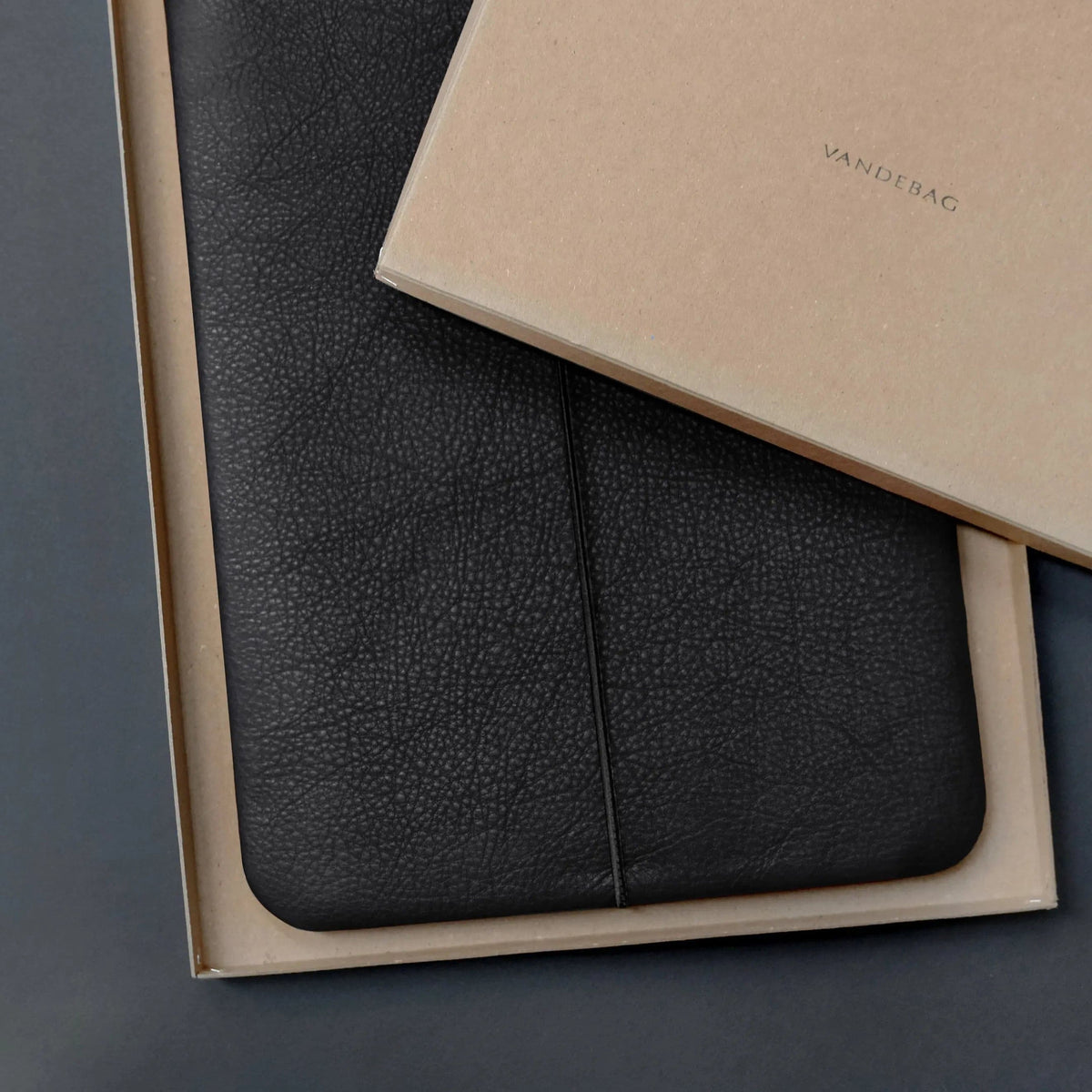 Macbookhülle aus schwarzem Rindsleder liegt in einer Geschenkbox auf der VANDEBAG steht